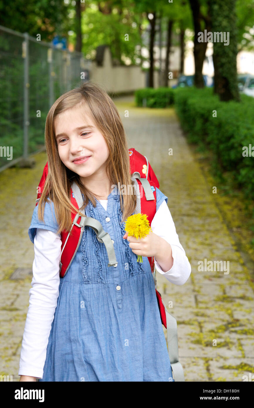 Petite fille qui marche à la maison de l'école, tenant une fleur, Munich, Bavière, Allemagne Banque D'Images