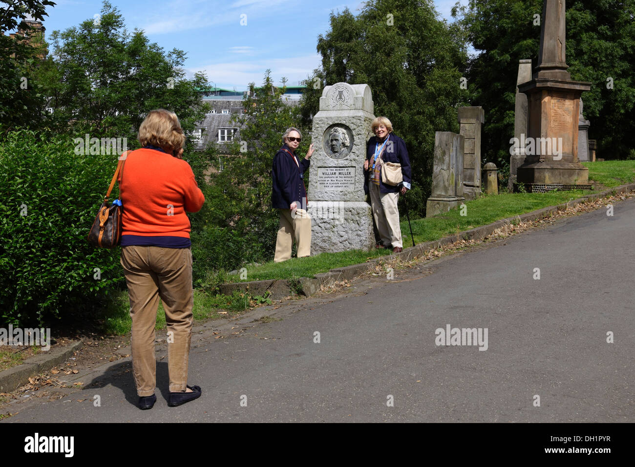 Touristes posant pour une photo à côté du mémorial à William Miller, Wee Willie Winkie auteur, Glasgow Necropolis, Écosse, Royaume-Uni Banque D'Images