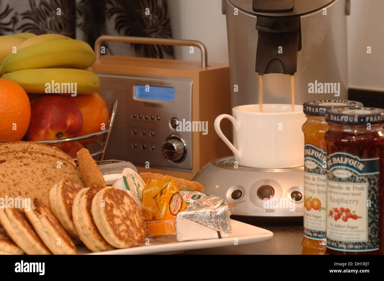 L'on verse du café pour un petit déjeuner contenant des gâteaux gallois confiture Confiture beurre Fromage fruit, il y a aussi une radio numérique. Banque D'Images