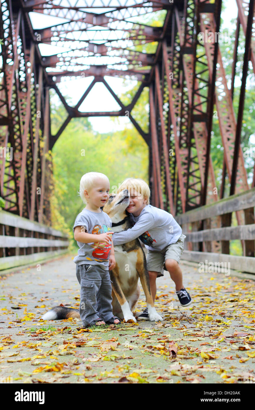 Deux jeunes enfants, un garçon et son petit frère comme à l'extérieur sur un pont dans les bois, serrant avec amour leur chien berger Banque D'Images