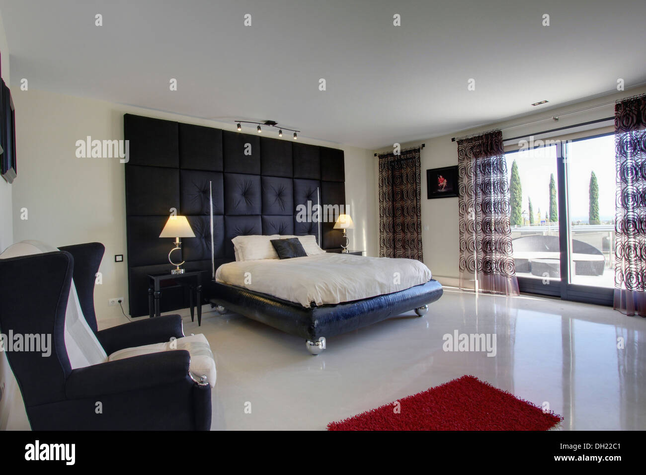 Faux mur capitonné noir boutonné derrière lit sur roulettes en espagnol  moderne chambre avec plancher en céramique blanche et portes en verre Photo  Stock - Alamy