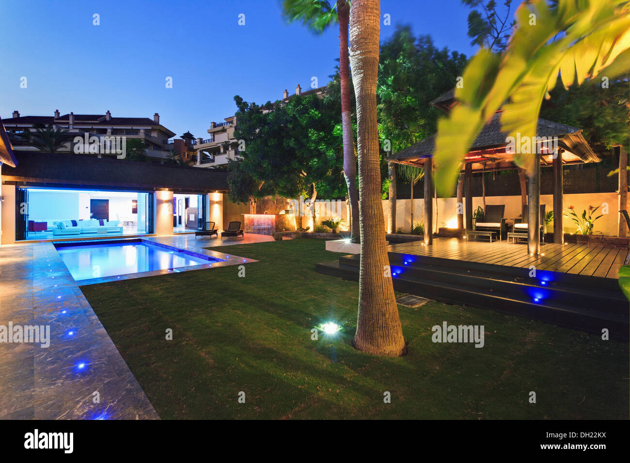 Palmier en pelouse à côté grande terrasse en bois et piscine dans jardin de Villa éclairée la nuit Banque D'Images