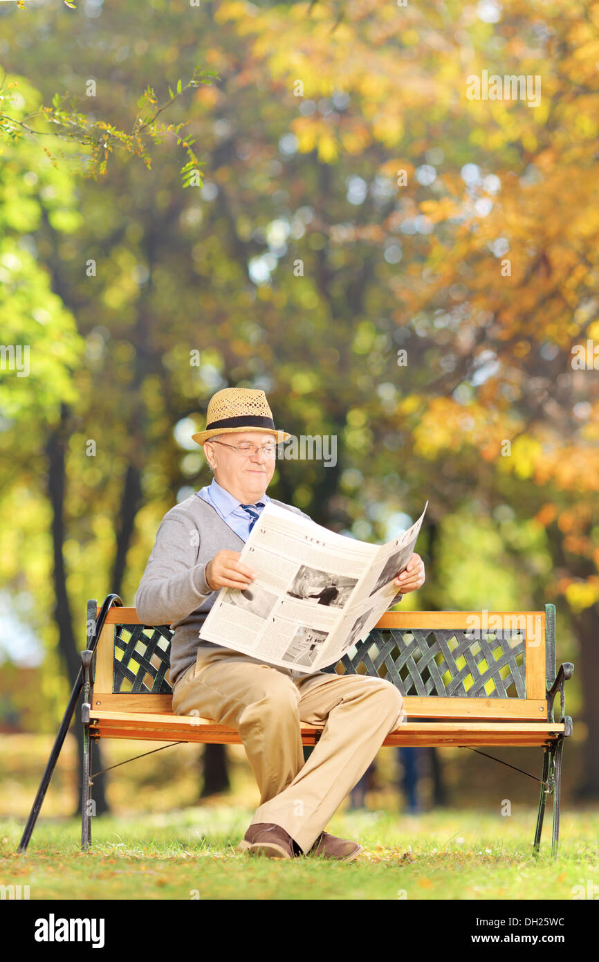 Représentant Senior assis sur un banc de lire le journal dans un parc en automne Banque D'Images