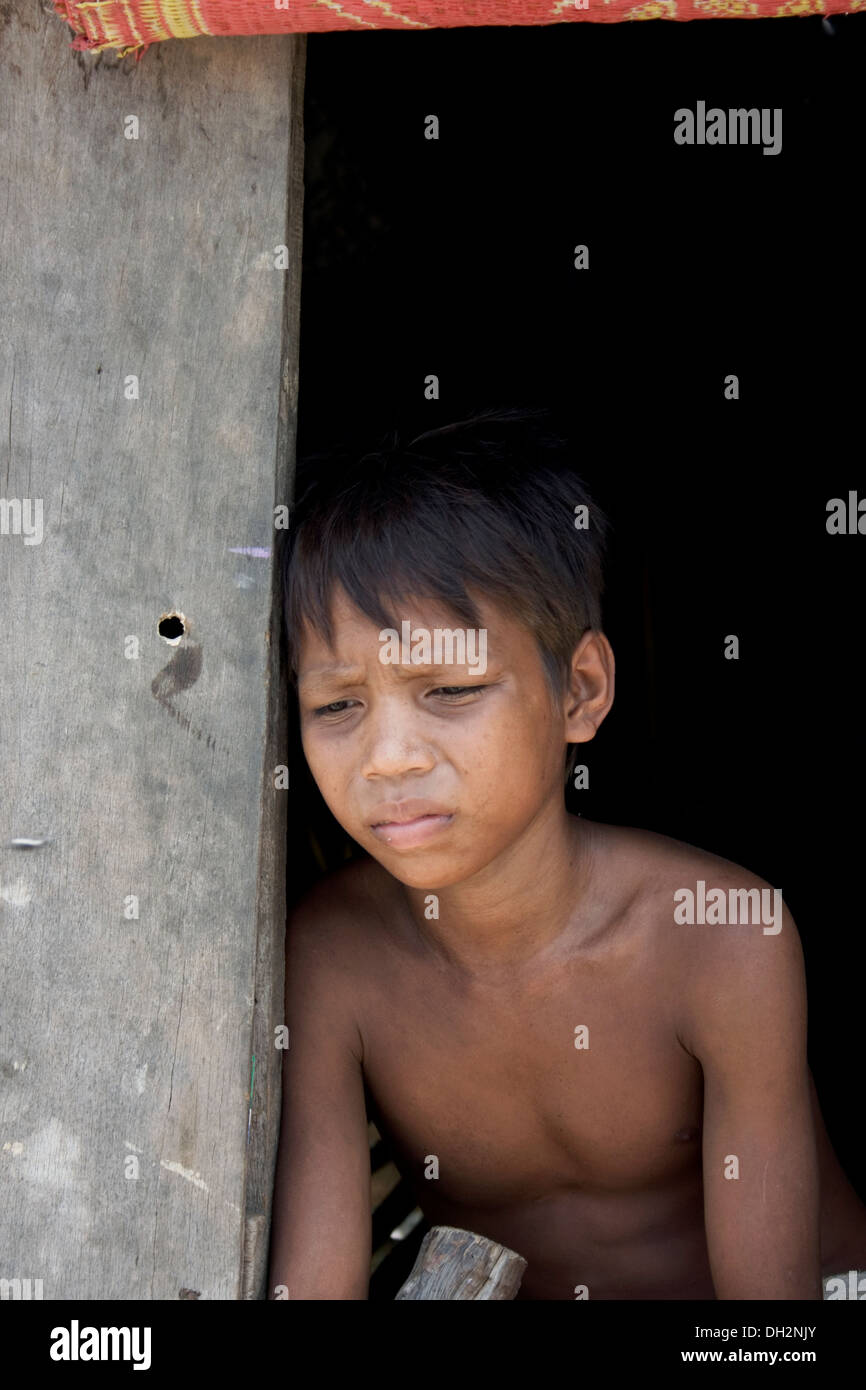 Un enfant travailleur garçon qui travaille dans l'industrie du recyclage est assis sur le seuil de sa maison en bois à Phnom Penh, Cambodge. Banque D'Images