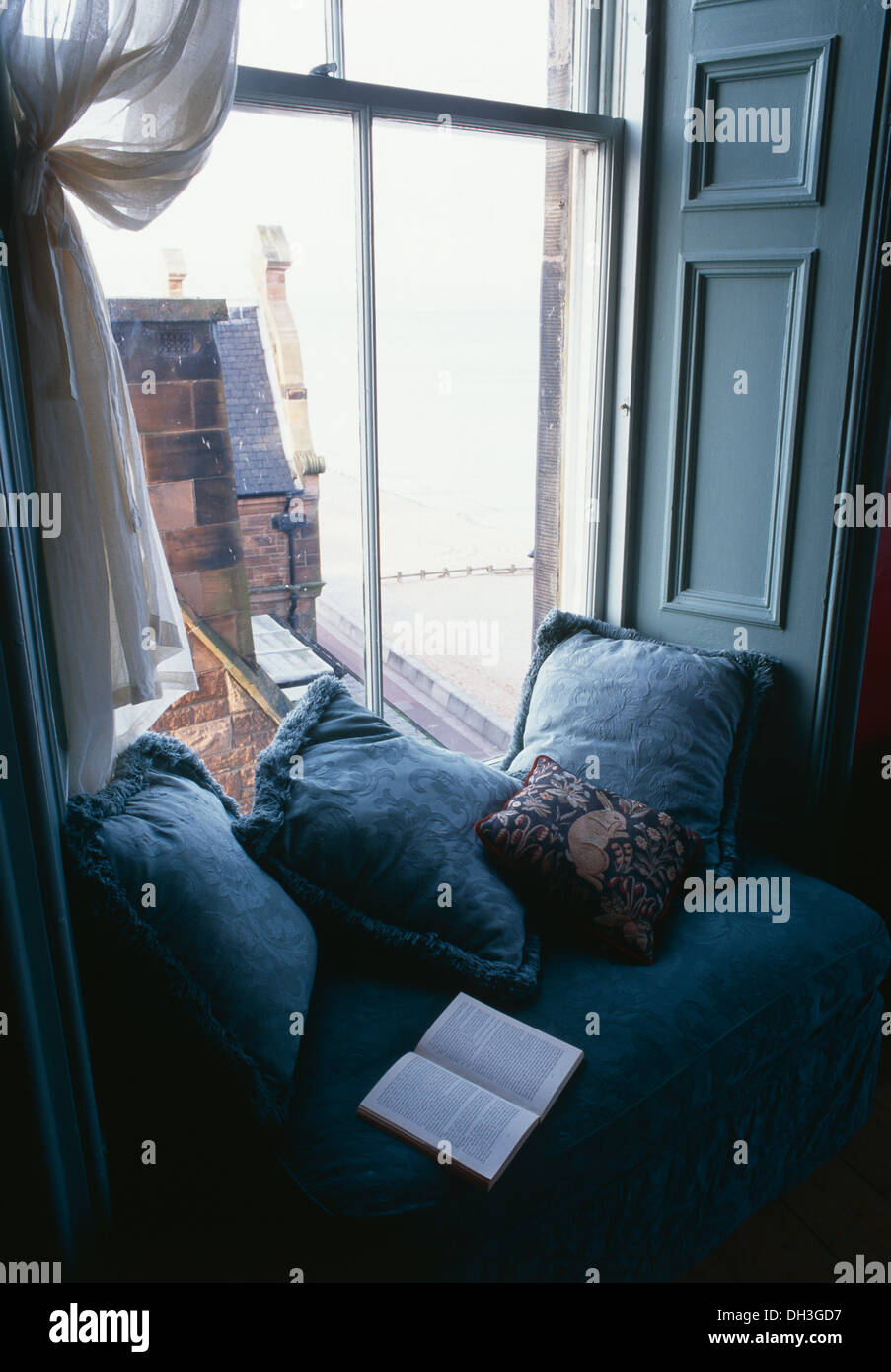 Rideaux de voile blanc avec coussins bleu et un livre ouvert sur un siège côté fenêtre bleu Banque D'Images