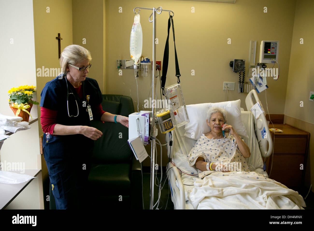 Infirmière blanc femme vérifie le liquide IV sac de 74 ans Hispanic woman in hospital bed Banque D'Images