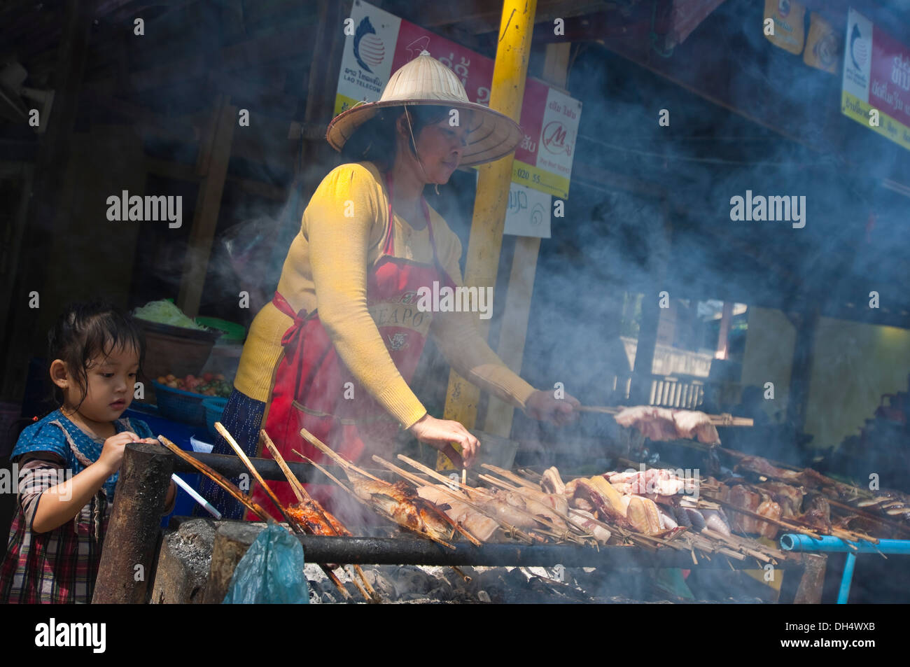 Portrait d'un horizontal dame Lao locale et sa fille griller les brochettes sur un barbecue au bord d'un restaurant. Banque D'Images