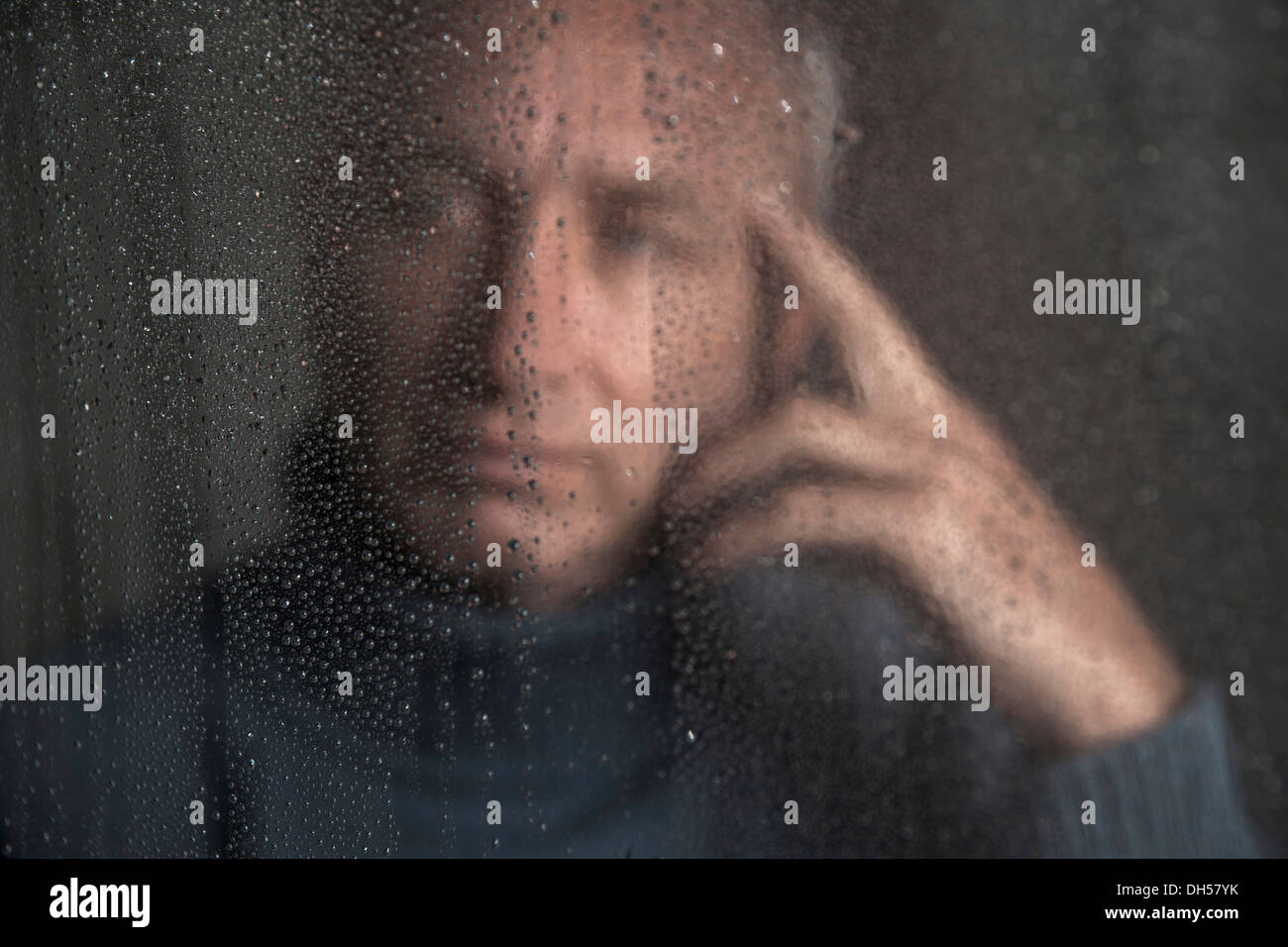 Homme seul assis derrière une fenêtre couverte de gouttes de pluie, Mannheim, Bade-Wurtemberg, Allemagne Banque D'Images