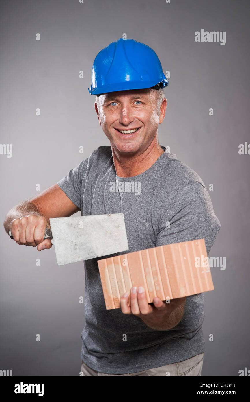 Travailleur de la construction portent un casque, tenant une truelle et une brique, Mannheim, Bade-Wurtemberg, Allemagne Banque D'Images