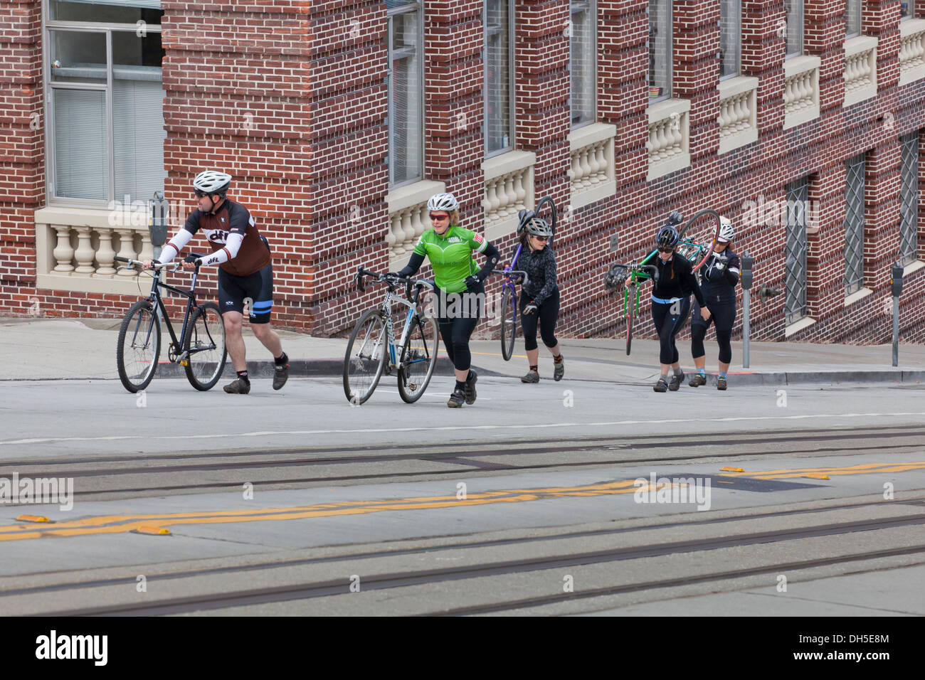 Les cyclistes des vélos de marche d'une rue en pente - San Francisco, California USA Banque D'Images