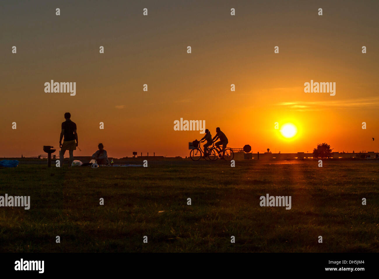 Couple having a barbecue sur l'Aérodrome de Tempelhof dans le soleil du soir en face de deux cyclistes de passage, Berlin-Tempelhof Banque D'Images