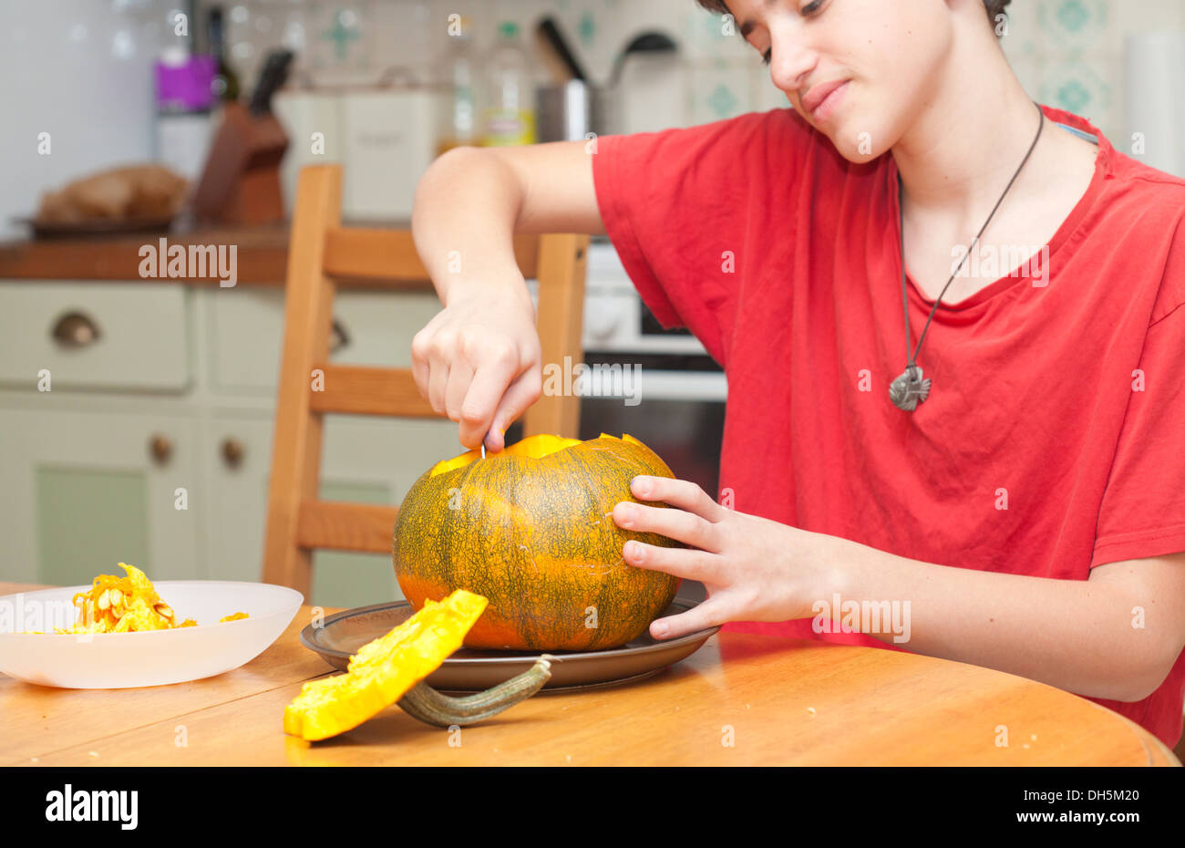 Un garçon sculptant la citrouille d'Halloween sur une table de cuisine, photo en candide Banque D'Images