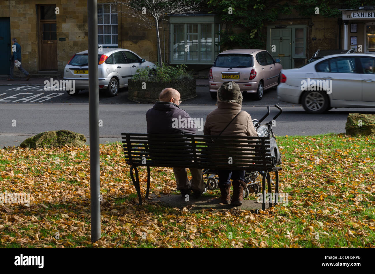 Un couple de personnes âgées assis sur un banc avec poussette entouré de feuilles mortes Banque D'Images