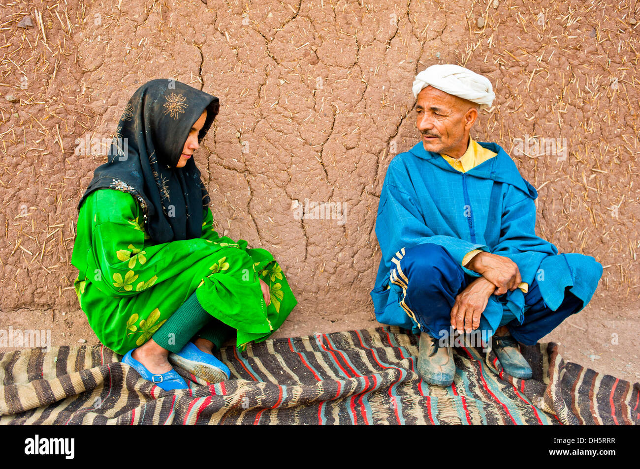 Un homme âgé et une jeune fille, peuple berbère, accroupis sur une moquette ou un tapis en face d'une chambre à parler de brique de boue Banque D'Images