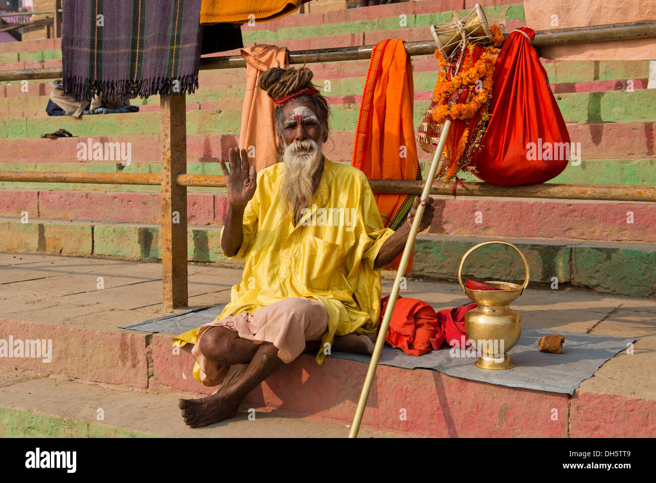 Personnes âgées Sadhu, saint homme ascète errant ou assis sur une couverture sur les étapes sur la rive de la rivière Ganges avec divers Banque D'Images