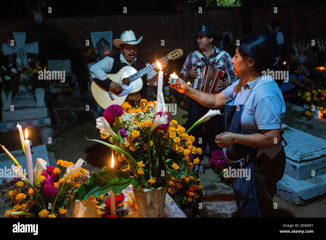 Une femme mexicaine s'allume des bougies sur la tombe d'un membre de la famille comme un Mariachi band joue pendant le jour de la fête des morts connus en espagnol comme d'un de muertos à l'ancien cimetière le 31 octobre 2013, au Mexique. Xoxocotlan dans Banque D'Images