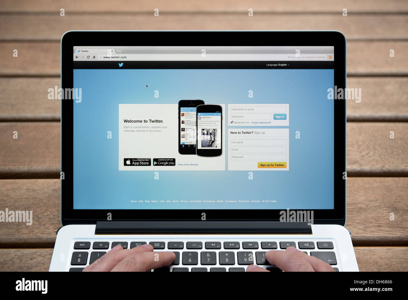 Le site web de Twitter sur un MacBook contre un banc en bois fond de plein air y compris les doigts d'un homme (usage éditorial uniquement). Banque D'Images