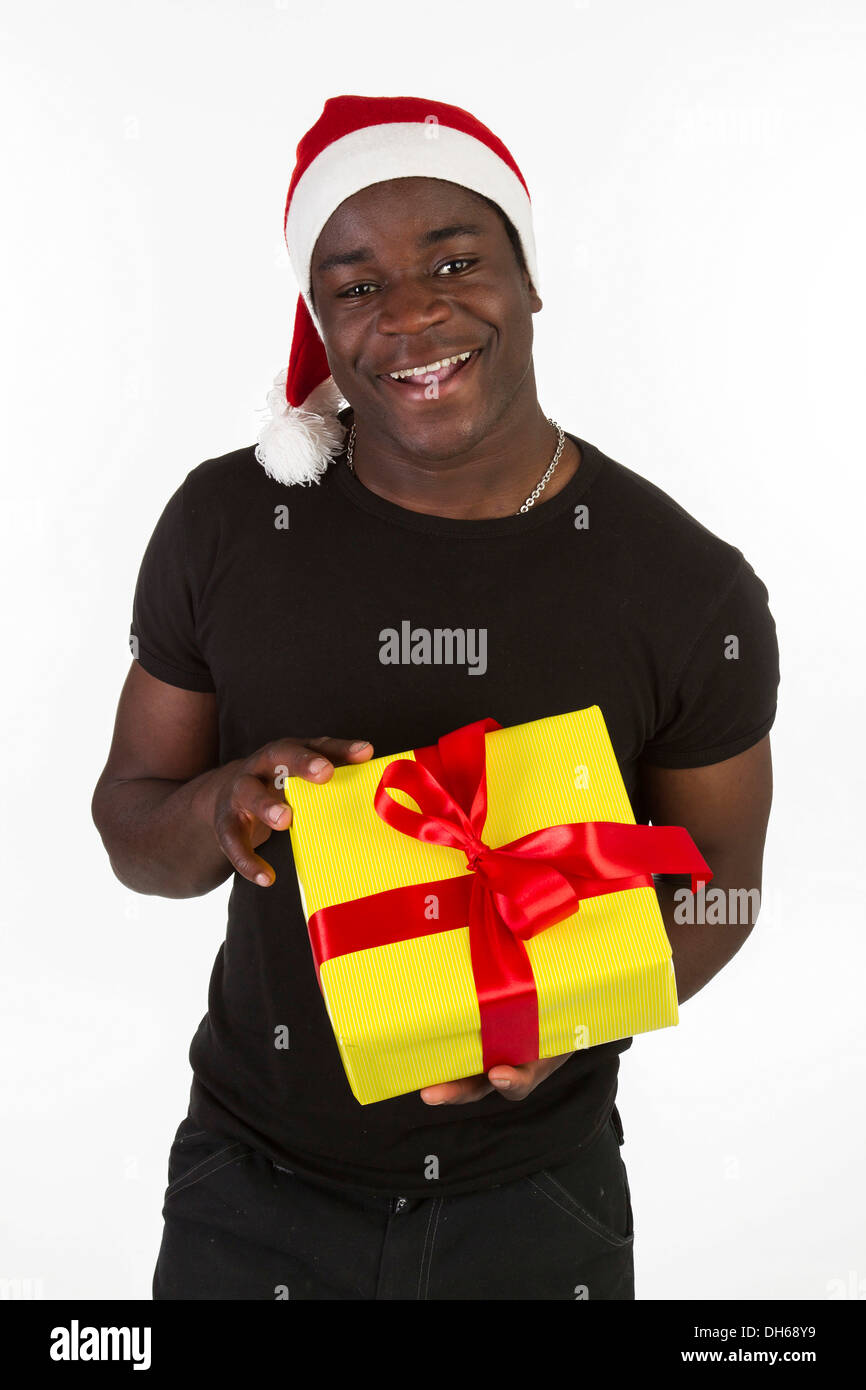 Jeune homme noir wearing a Santa hat and holding a present Banque D'Images