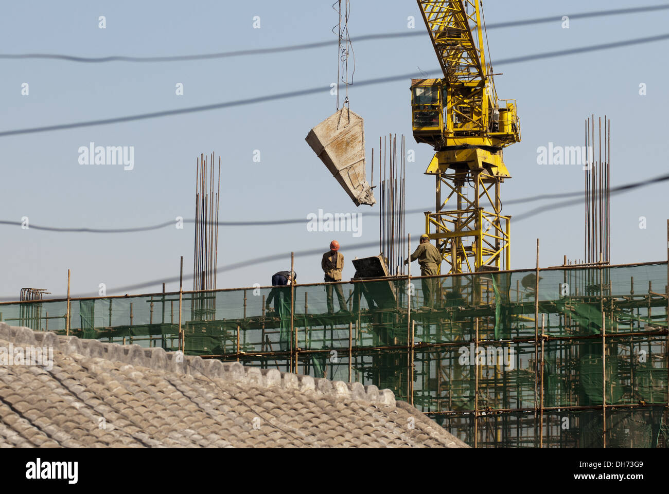 Les constructeurs qui utilisent une grue pour charger du ciment sur un chantier de construction à Pékin, tout en travaillant à construire un nouveau bâtiment soutenu par des échafaudages. © Olli Geibel Banque D'Images