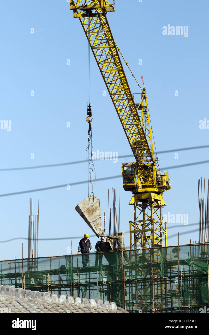 Les constructeurs qui utilisent une grue pour charger du ciment sur un chantier de construction à Pékin, tout en travaillant à construire un nouveau bâtiment soutenu par des échafaudages. © Olli Geibel Banque D'Images