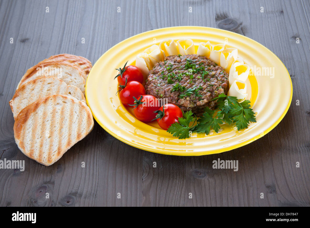 Steak tartare avec du pain grillé, des tomates et du beurre sur la plaque jaune Banque D'Images