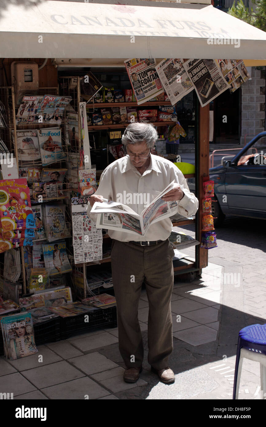 Vieil homme lisant un journal à un kiosque de la rue. La Crète. Banque D'Images