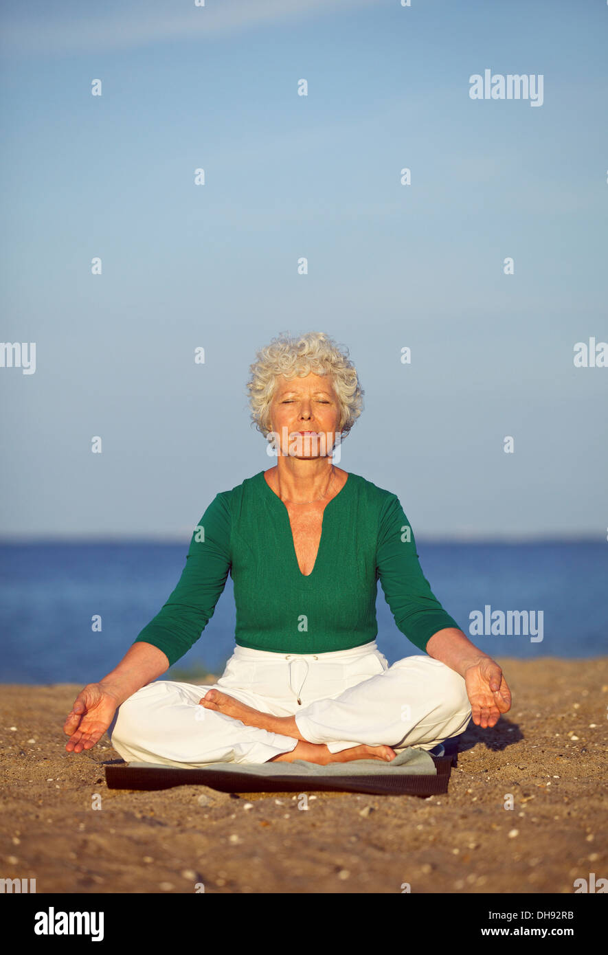 Portrait de la femme senior en méditant sur le bord de la mer. Vieille Femme se détendre par la mer faisant du yoga. La méditation, yoga et relaxation Banque D'Images