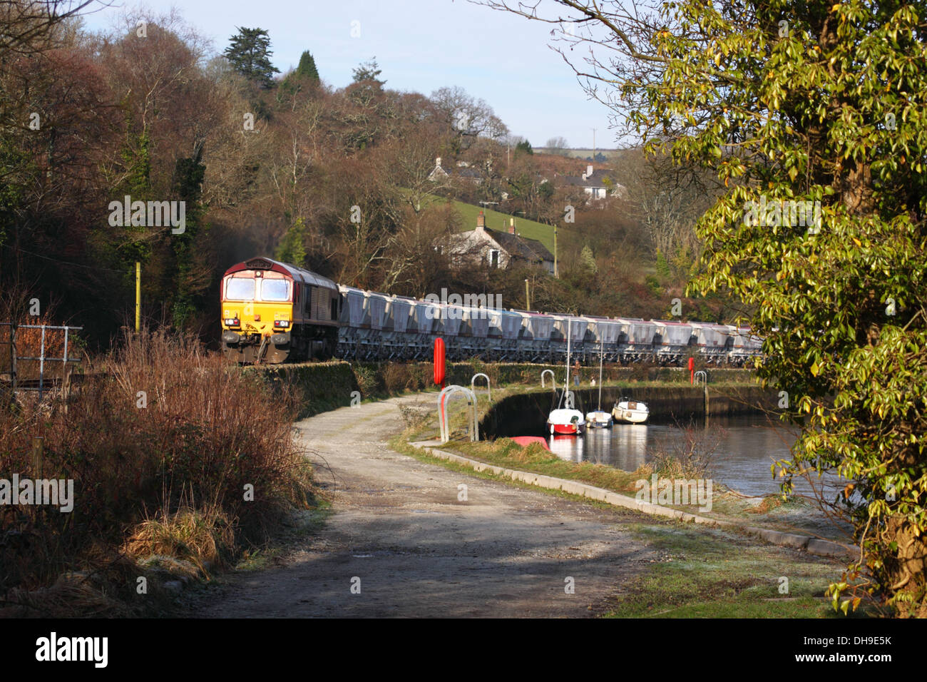 Un diesel trains remorqués de kaolin wagons passe d'une rivière avec des bateaux amarrés. Banque D'Images