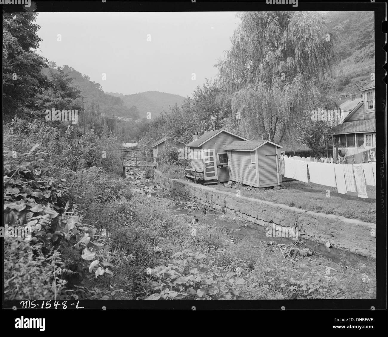 Cette image représente des arrière-cours avec des prieurés et des maisons de charbon, communes dans de nombreuses maisons rurales au début du XXe siècle. La photographie souligne la présence de toilettes extérieures et l’entretien de la rive du ruisseau, reflétant l’infrastructure de l’époque. Banque D'Images