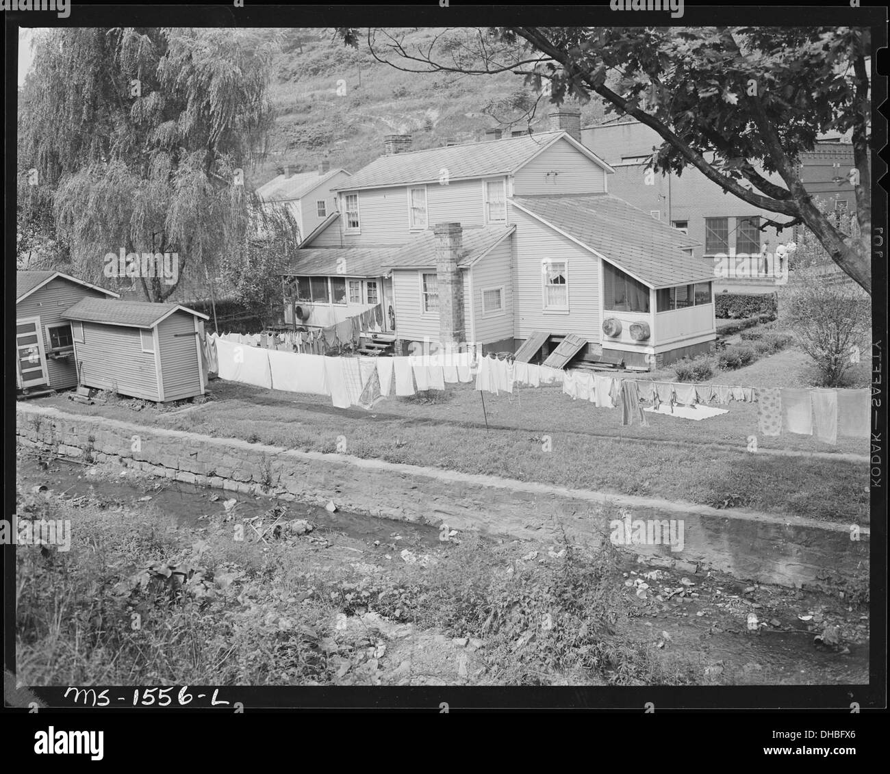 Cette photographie représente les arrière-cours de maisons avec des prieurés et des maisons de charbon, montrant l'entretien d'une rive de ruisseau. Les toilettes extérieures étaient courantes dans les zones rurales pendant cette période, soulignant les conditions de vie de base dans ces communautés. Banque D'Images