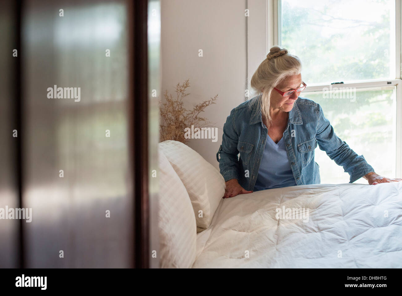 Une ferme à la campagne, une femme qui forment un lit dans une chambre. Banque D'Images