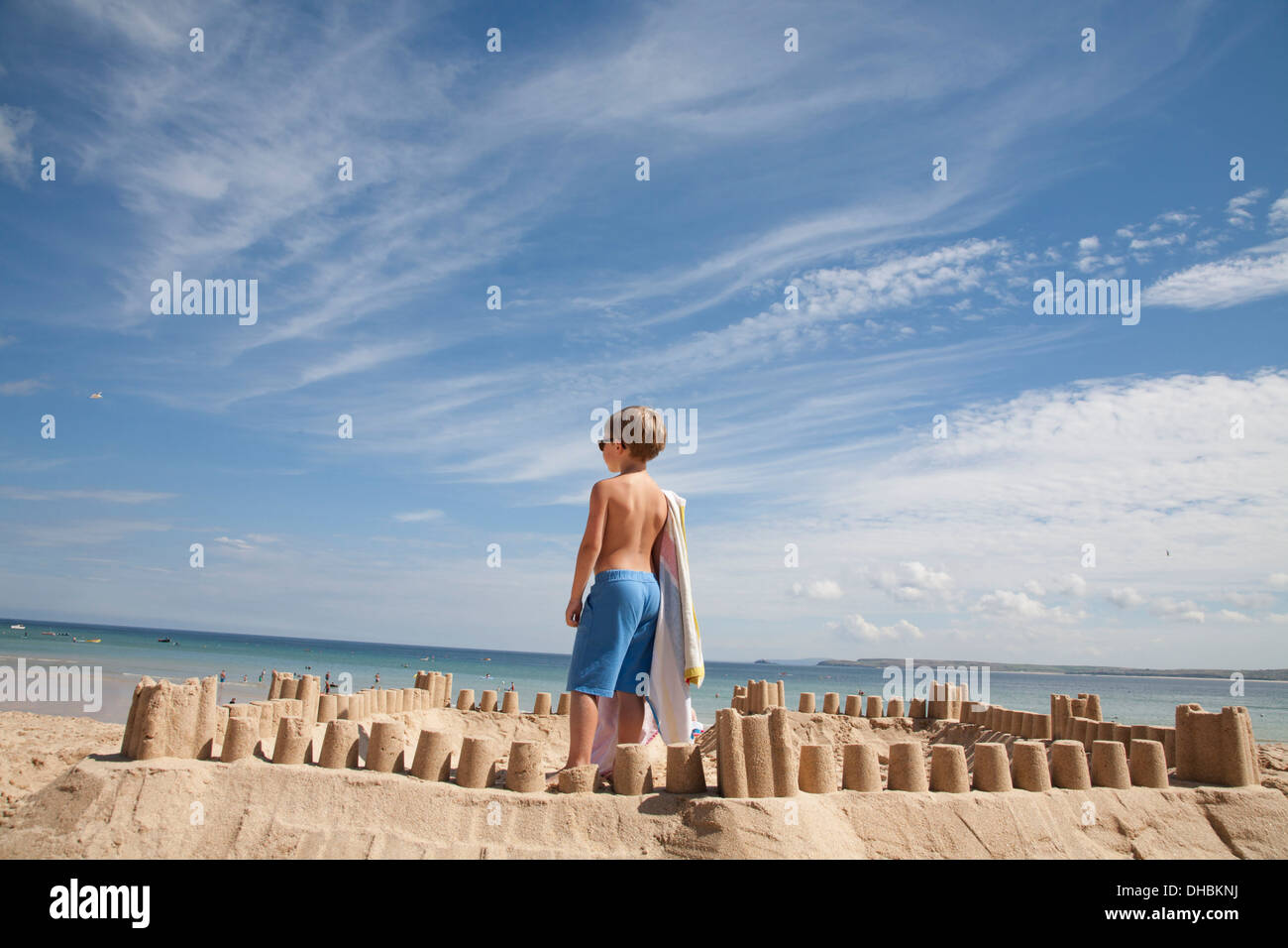 Un garçon debout à côté d'un château de sable, au sommet d'un monticule de sable. Plage. Banque D'Images