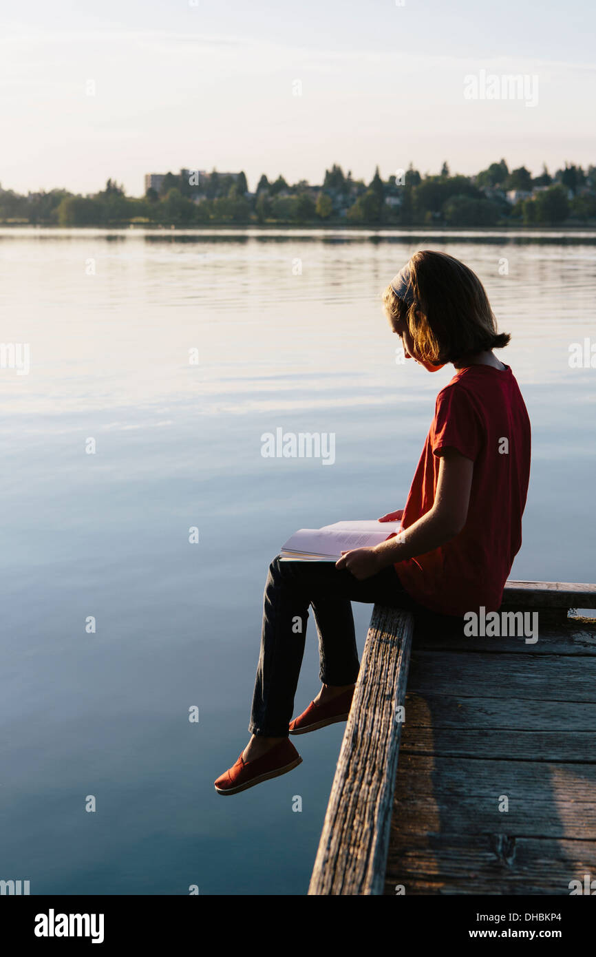Une jeune fille assise sur un quai, la lecture d'un livre. Banque D'Images