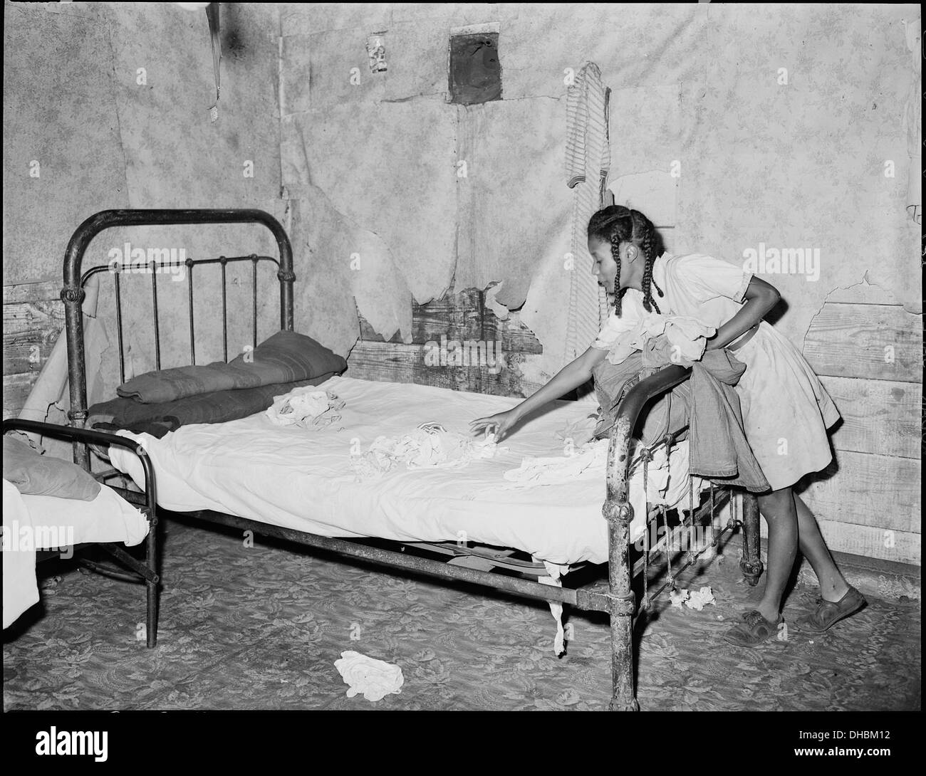 La fille de Lawson Mayo, un mineur handicapé, est vue en train de faire le lit dans la maison familiale de quatre pièces. La famille de douze vit dans des conditions modestes, reflétant les défis de la vie dans l'Amérique rurale au début du XXe siècle. Banque D'Images
