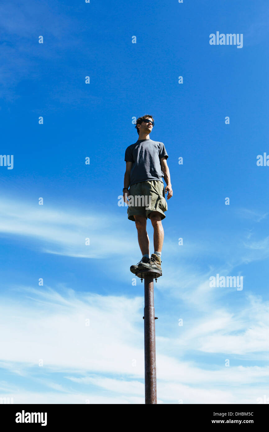 Homme debout en équilibre sur métal à la grande surprise du ciel vers les lacs alpins de montagne désert Mt Banque D'Images