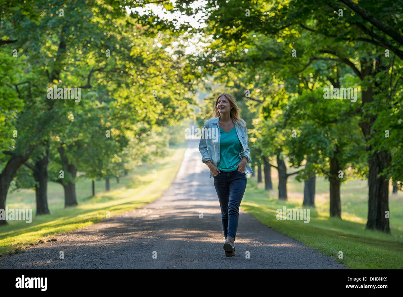Une femme marchant dans un chemin bordé d'arbres. Banque D'Images