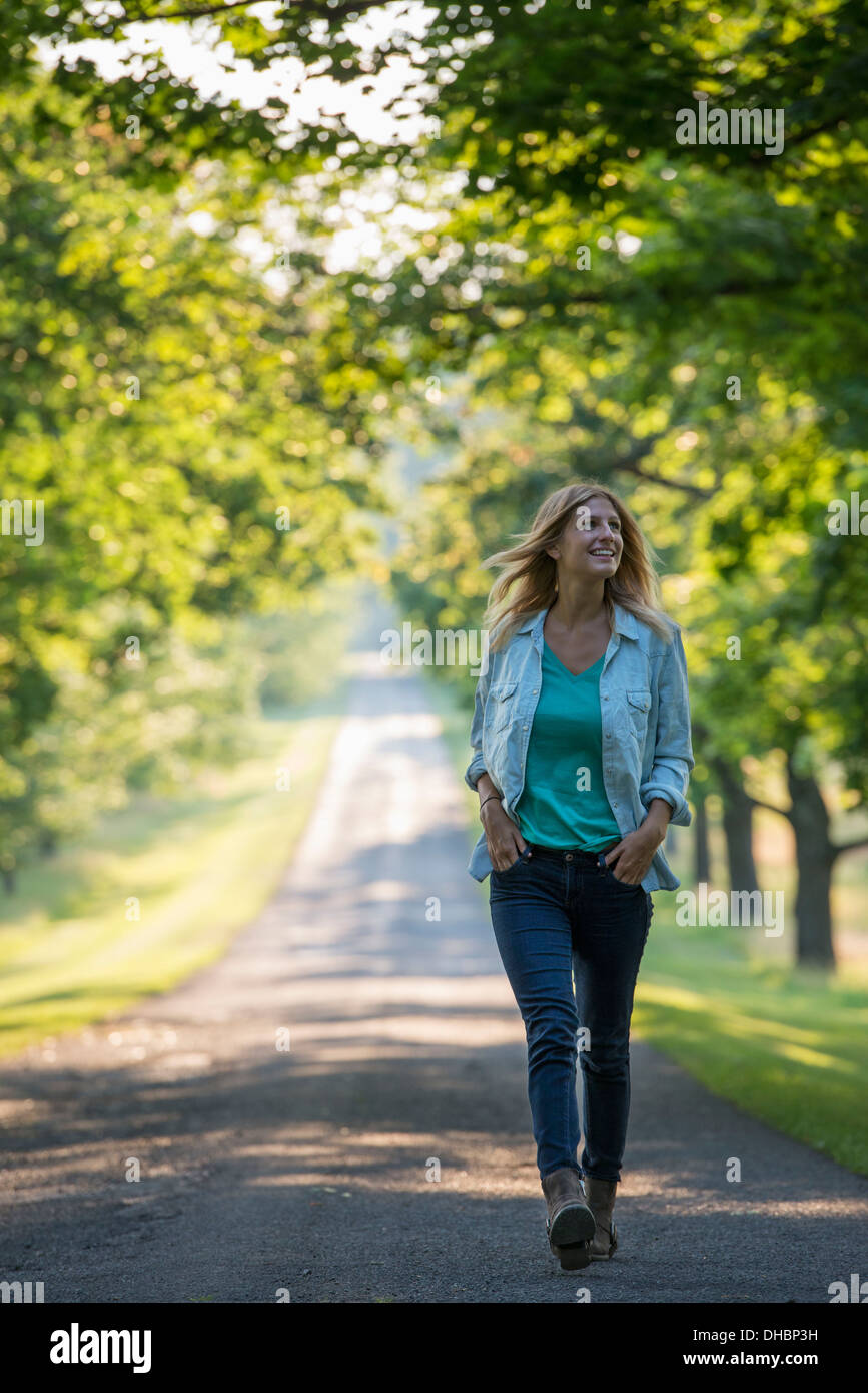 Une femme marchant dans un chemin bordé d'arbres. Banque D'Images