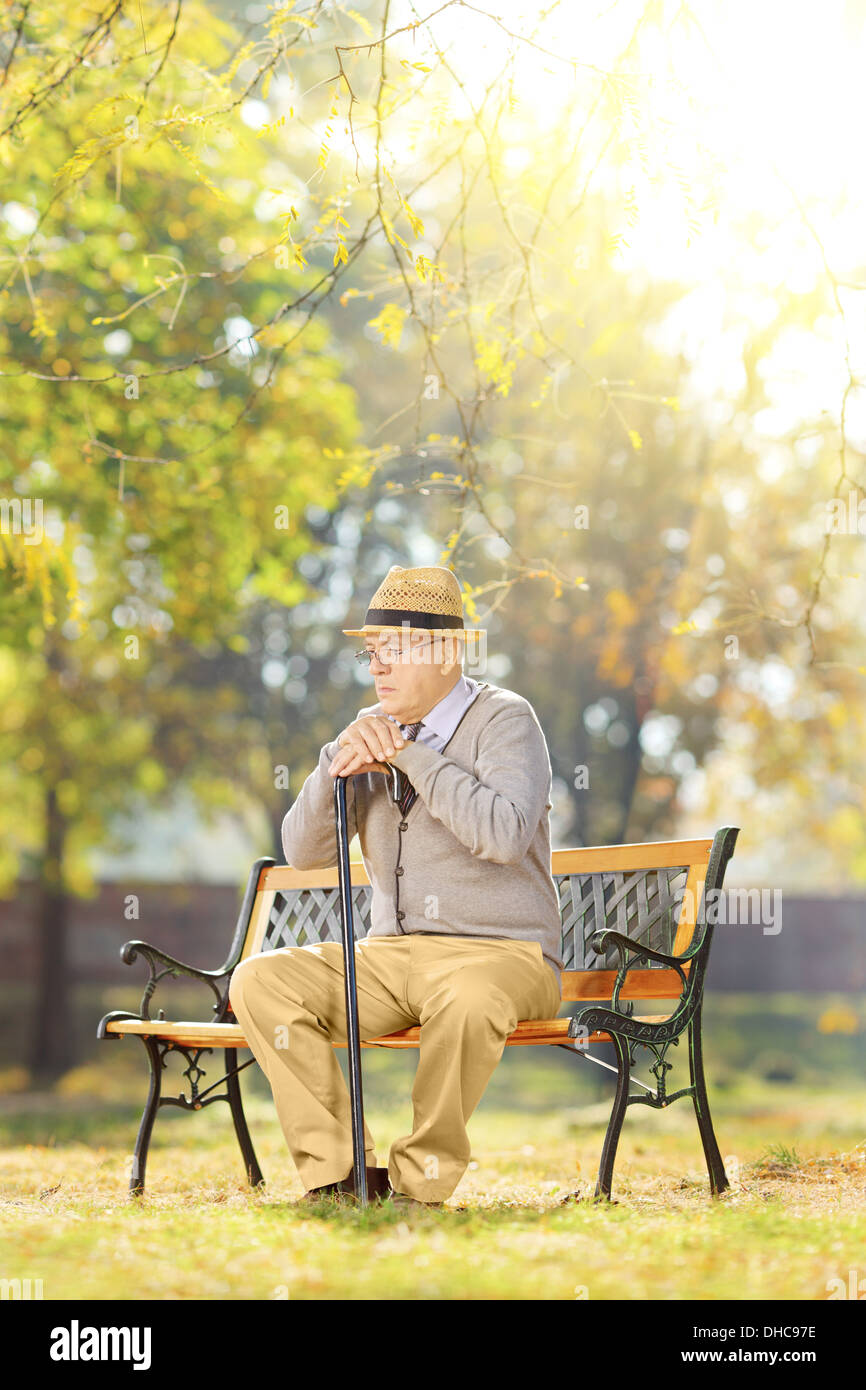 Senior triste monsieur avec une canne assis sur banc en bois dans un parc Banque D'Images