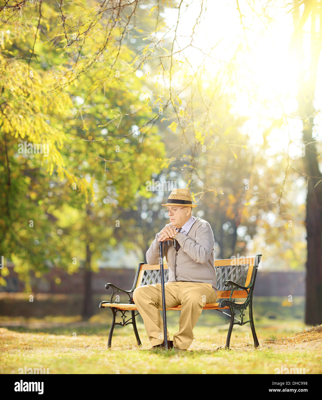 Sad man avec une canne assis sur banc en bois dans un parc sur une journée ensoleillée Banque D'Images