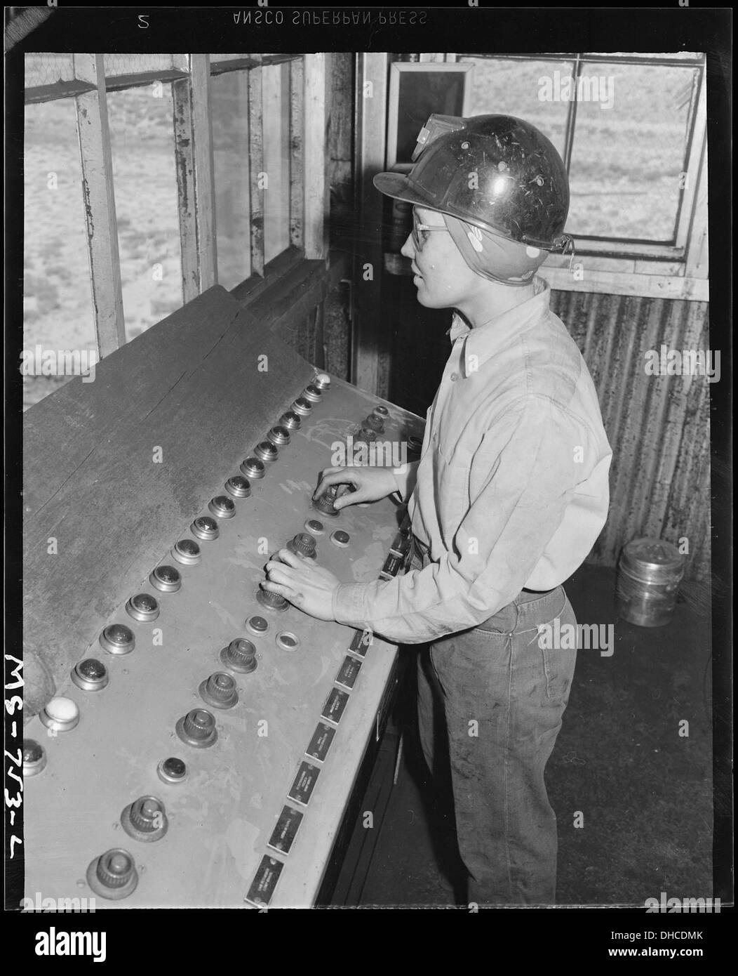 Cette photographie représente une jeune fille actionnant un système de boutons-poussoirs pour contrôler le chargement de charbon dans les wagons de chemin de fer. La scène fait partie du travail industriel, montrant l'utilisation de systèmes mécaniques pour la manutention de matériaux. Banque D'Images