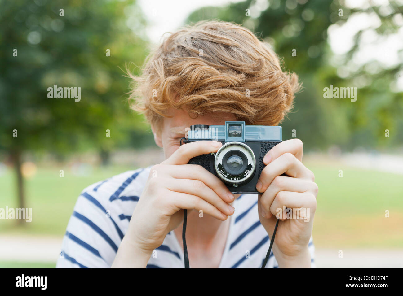 Jeune homme de prendre une photo en parc avec un appareil photo à l'ancienne Banque D'Images