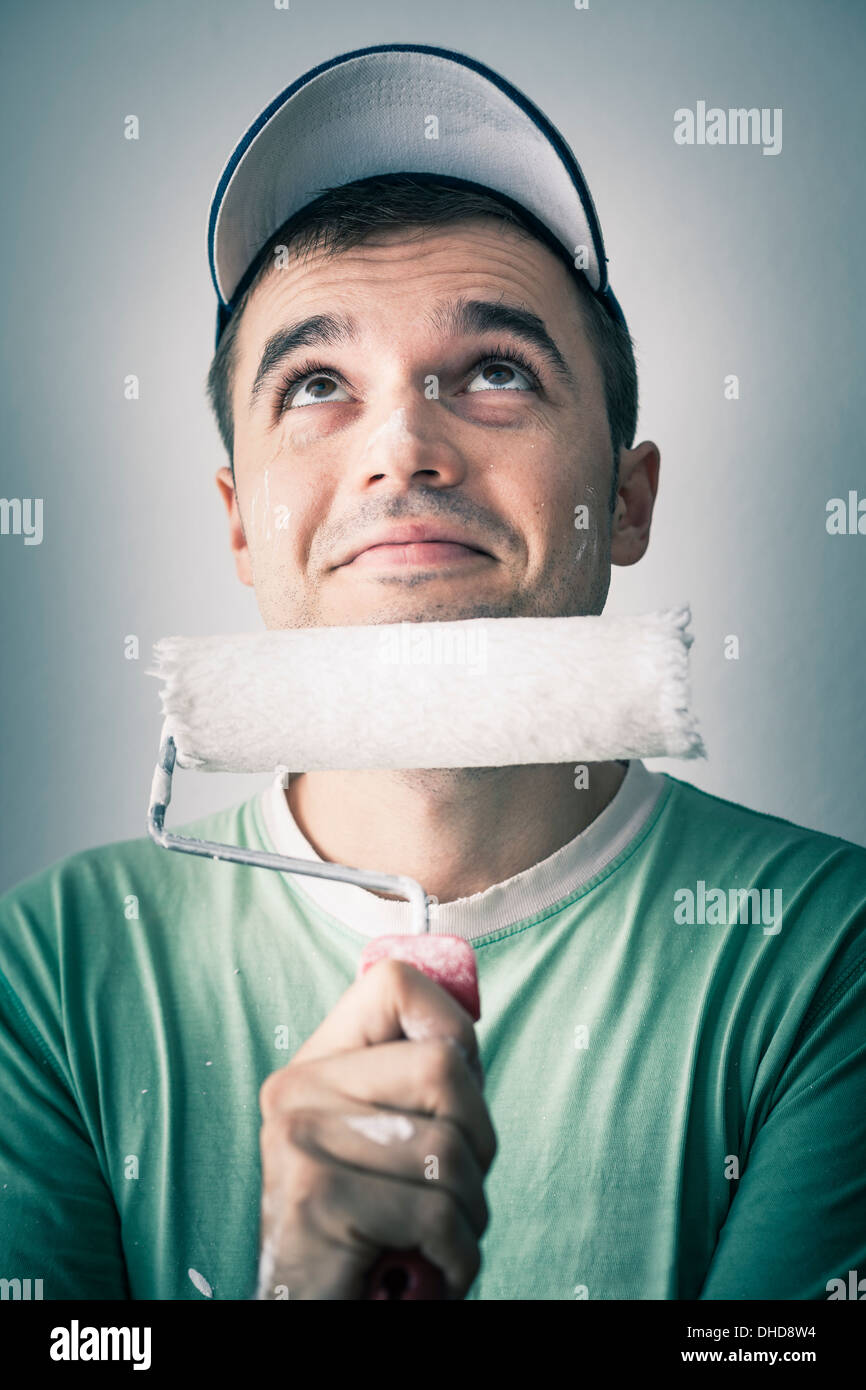 L'homme créatif smiling réfléchie avec rouleau à peindre jusqu'à la recherche. Banque D'Images