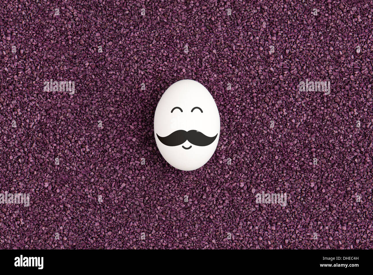Un seul œuf avec moustache sont couchés sur le sable violet décoratif et souriant. Banque D'Images