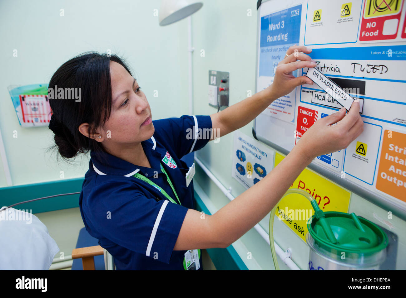 Une femme infirmière philippine modifie les informations du patient au-dessus d'un lit de NHS UK Banque D'Images