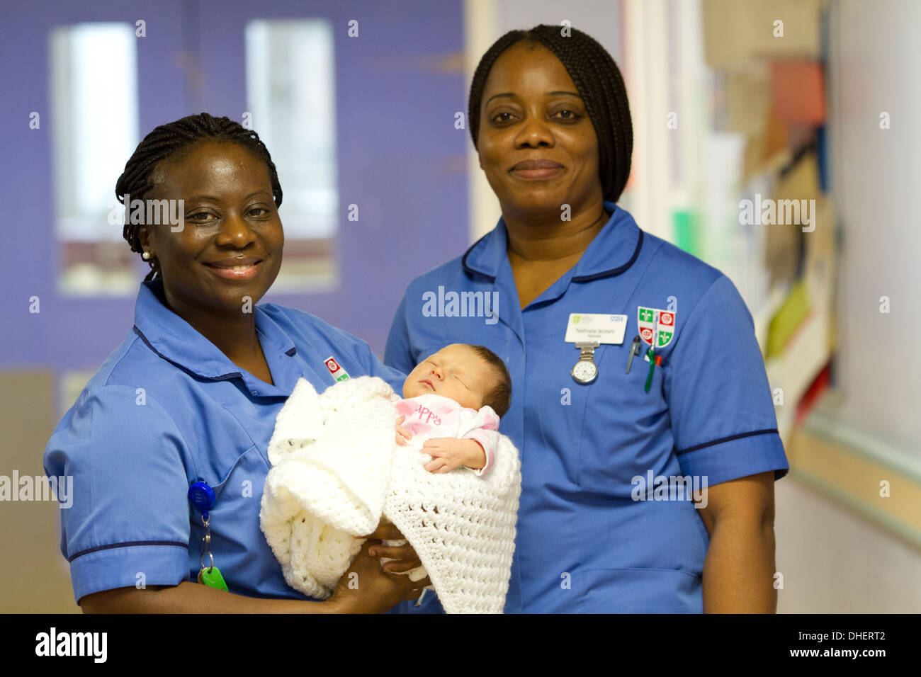 Une sage-femme est titulaire d'un bébé nouveau-né tandis qu'un collègue s'en tient dans un couloir de l'hôpital UK Banque D'Images