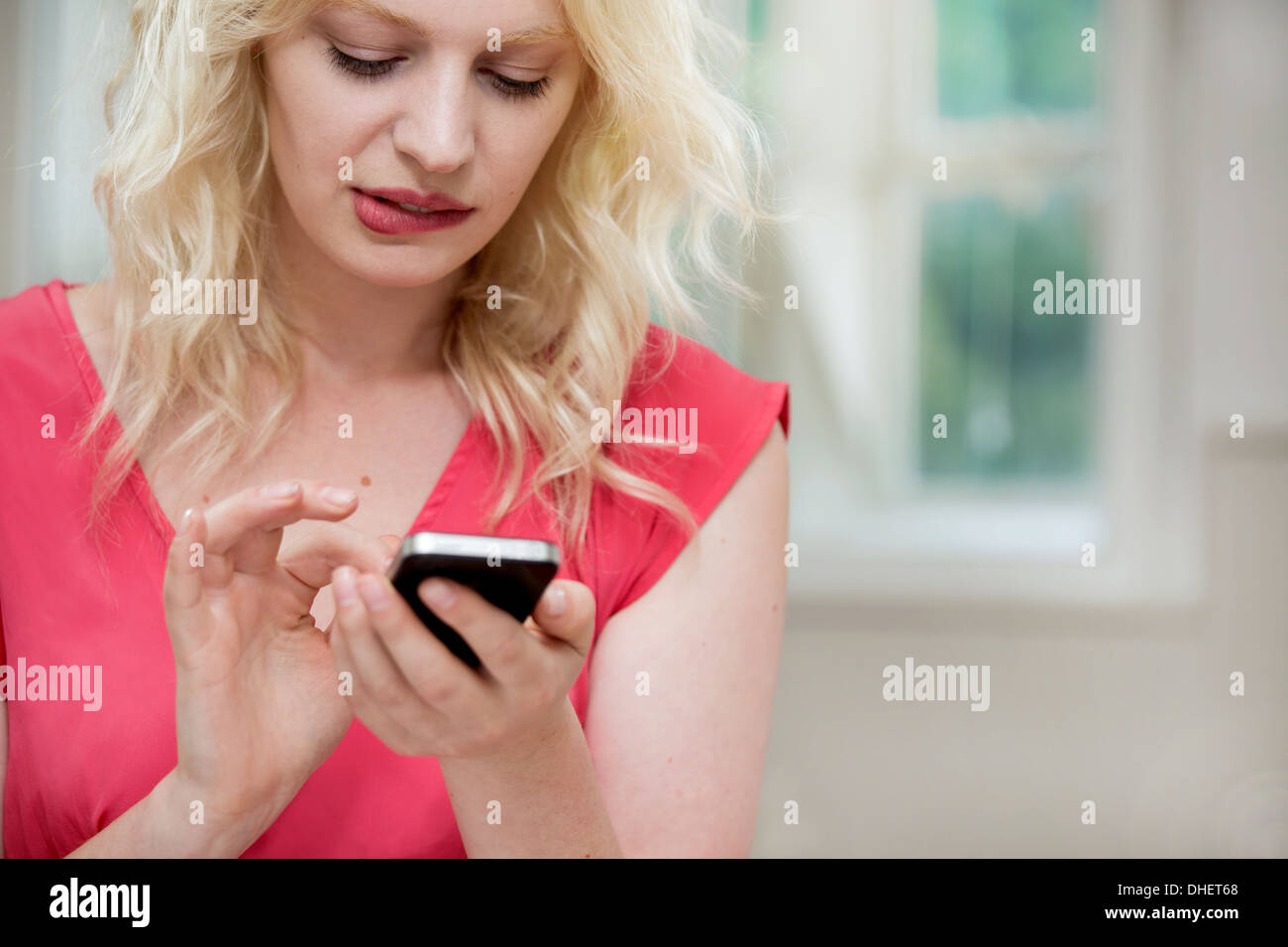 Young woman using smartphone, biting lip Banque D'Images