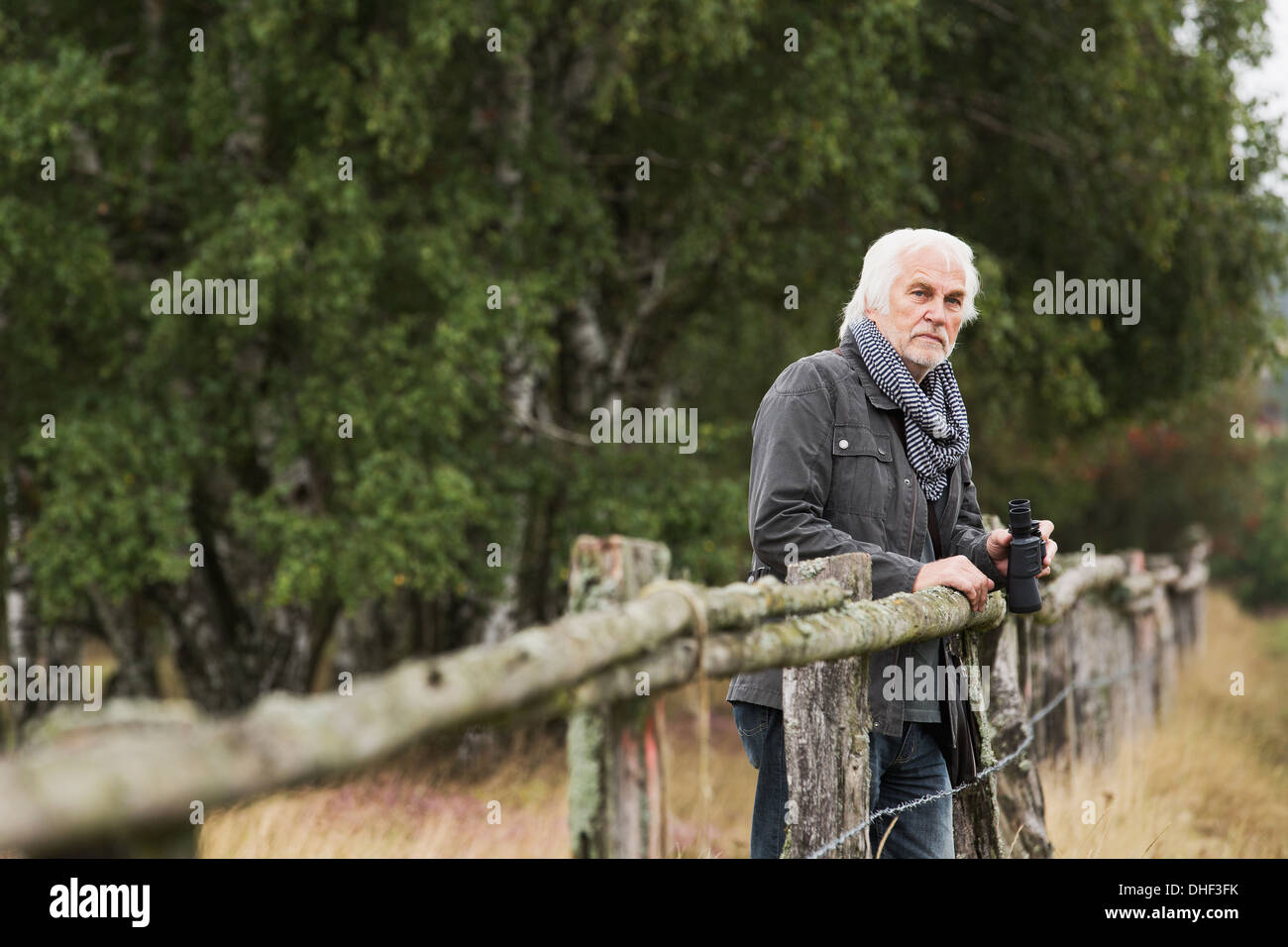 Senior man leaning on wooden fence with binoculars Banque D'Images Senior man leaning on wooden fence with binoculars Banque D'Images