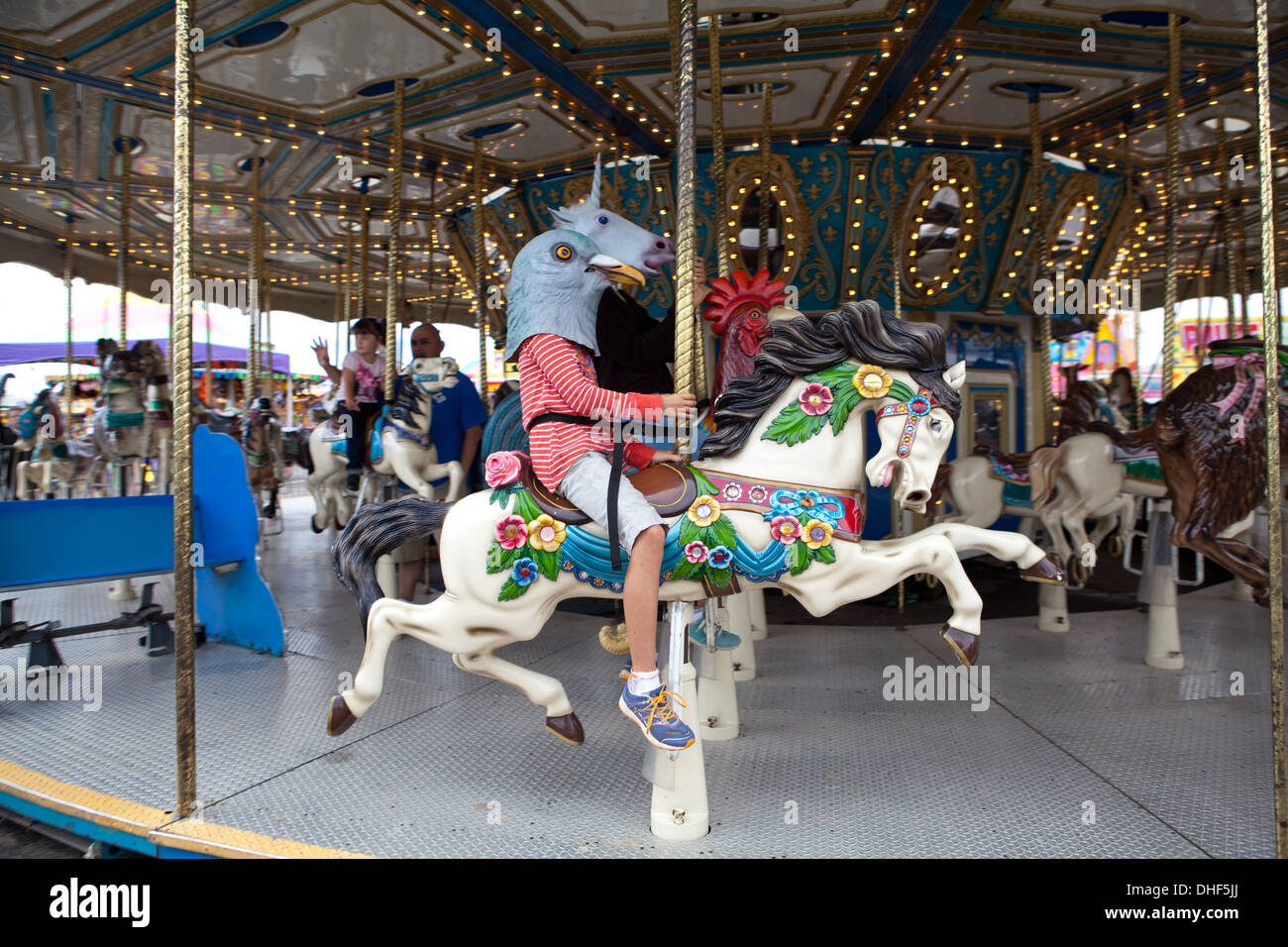 Les enfants portant des masques d'animaux à cheval sur un carrousel ride at state fair. Banque D'Images