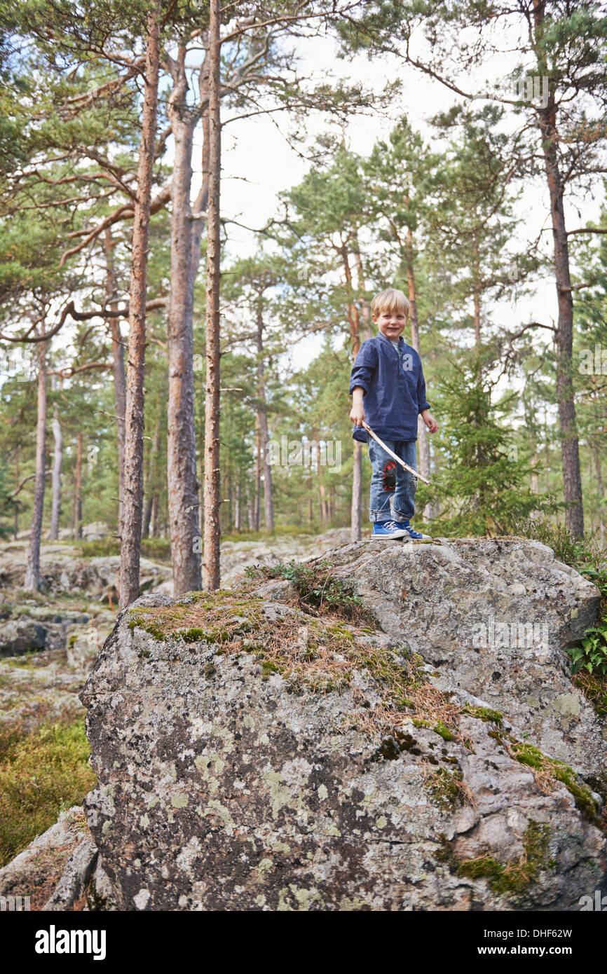 Boy standing on rocks holding stick Banque D'Images