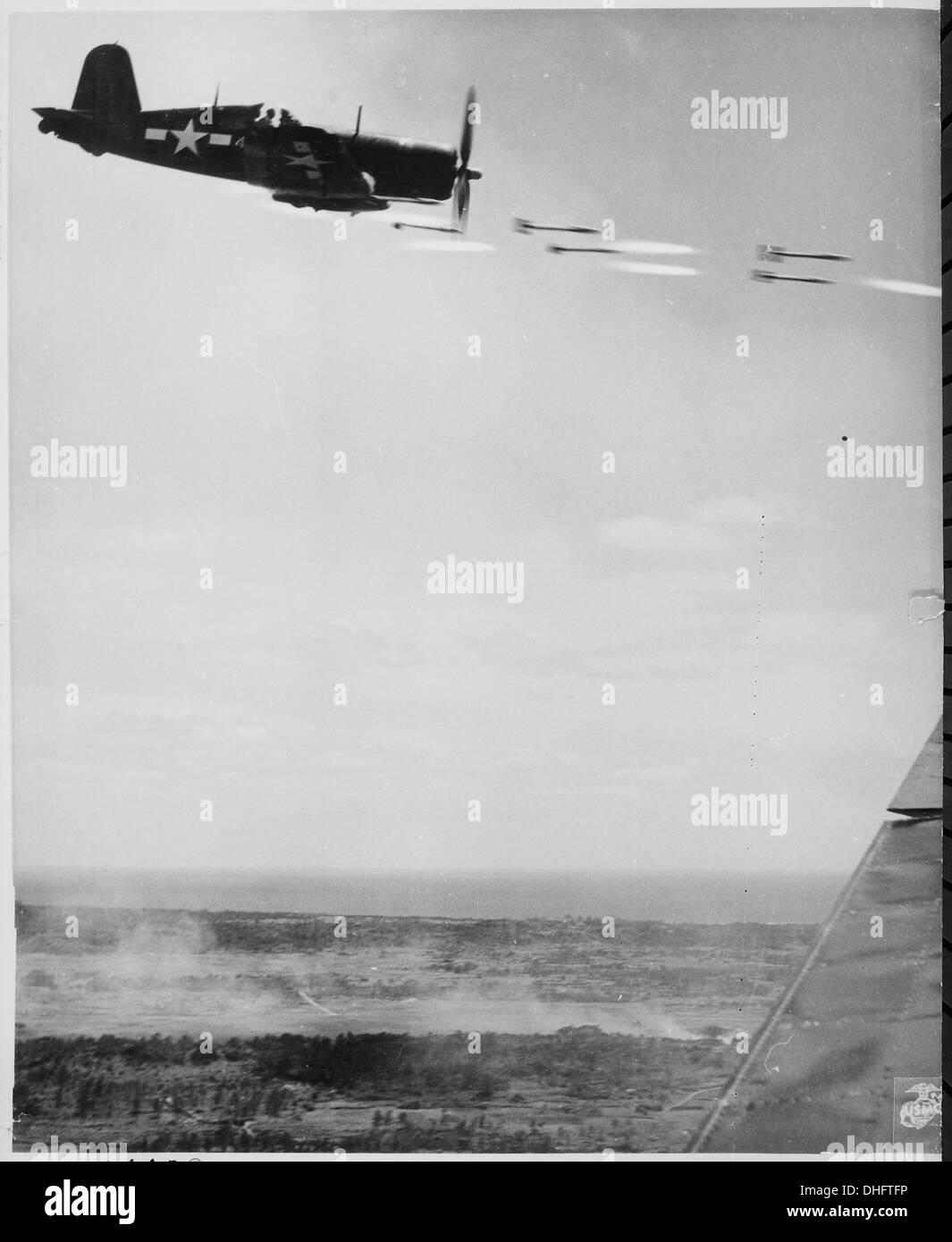 Un chasseur Corsair lâche ses projectiles de fusée lors d'une course au-dessus d'Okinawa, ciblant un bastion japonais pendant la seconde Guerre mondiale, avec des explosions en arrière-plan. Banque D'Images